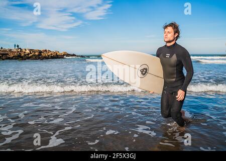 Surfeur laissant l'eau avec planche de surf sous son bras. Banque D'Images