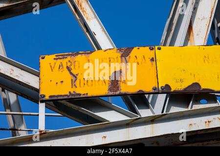 Vieux panneau d'avertissement jaune rouillé sur la structure de la grue de quai contre le ciel bleu clair dans le district de Jätkäsaari ou de Länsisatama à Helsinki, en Finlande Banque D'Images