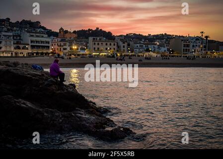 L'homme tient une canne à pêche tandis que le soleil se couche au village maritime de Tossa de Mar, province de Gérone, Espagne. Banque D'Images