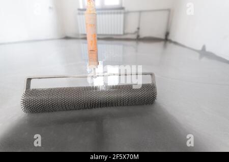 Nivellement avec un mélange de sols en ciment. Époxy auto-nivelant avec rouleau à aiguilles. Rouleau à pointes pour plancher en vrac. Banque D'Images