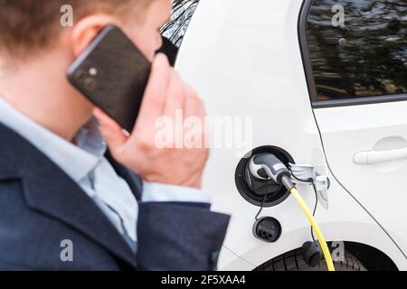 Homme chargé une voiture électrique et parlant sur le smartphone. Concept de voiture ECO EV Banque D'Images