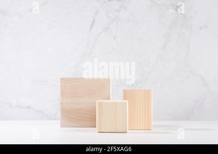 Podiums beige en bois de forme carrée dans un élégant intérieur blanc avec un mur en marbre gris dans une lumière solaire pour l'exposition de produits cosmétiques. Banque D'Images