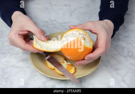 Les mains de l'homme s'écaillent une orange. Concept d'alimentation saine Banque D'Images