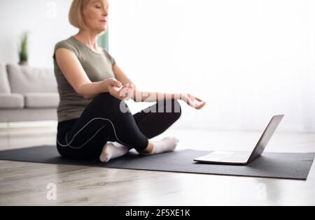 Femme mûre équilibrée méditant avec les yeux fermés devant l'ordinateur portable à la maison, foyer sélectif Banque D'Images