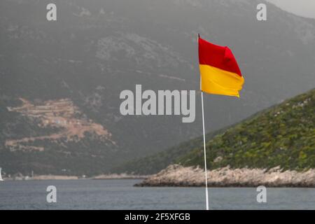 Un drapeau rouge et jaune qui saute la vie au bord de la mer. Banque D'Images