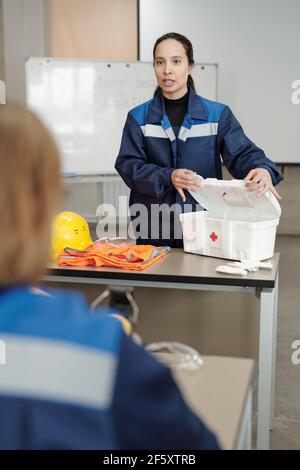 Jeune femme confiante dans un conteneur d'ouverture avec des produits médicaux tout en étant debout devant les collègues pendant les bases de la vie leçon de sécurité Banque D'Images