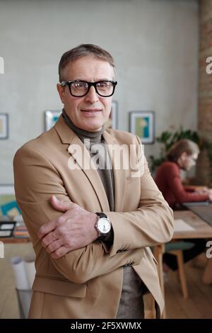 Architecte homme mature et réussi en vêtements décontractés et lunettes debout contre les jeunes collègues travaillant devant l'ordinateur Banque D'Images