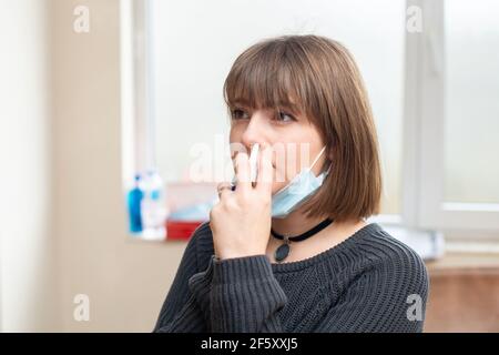 Jeune femme malade utilisant un spray nasal pour la protection contre le coronavirus pendant qu'elle est au travail. Banque D'Images