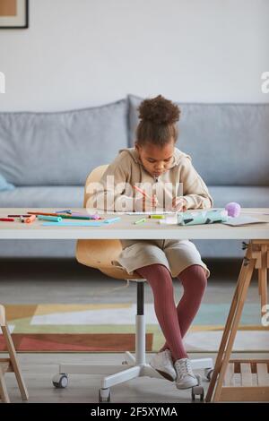 Portrait vertical pleine longueur d'une jolie fille afro-américaine tout en étant assis à une table dans un intérieur confortable, espace de copie Banque D'Images