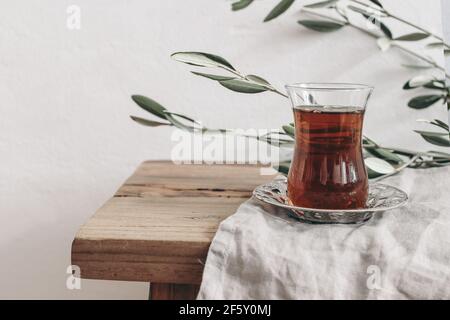 Gros plan du thé noir turc en verre sur la soucoupe argentée. Carte de vœux de Ramadan Kareem, invitation. Branches d'olivier vertes sur une ancienne table en bois Banque D'Images