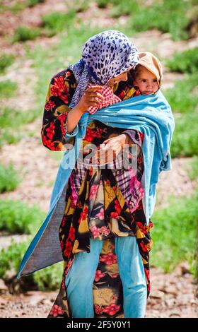 Zaida, Maroc - 10 avril 2015. Berberbère femme en vêtements traditionnels portant une jolie fille sur le dos Banque D'Images