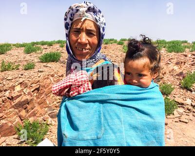 Zaida, Maroc - 10 avril 2015. Berberbère femme en vêtements traditionnels portant une jolie fille sur le dos Banque D'Images