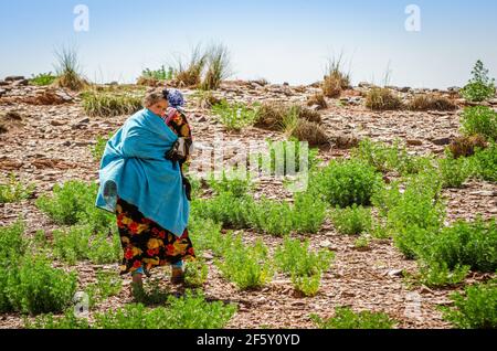 Zaida, Maroc - 10 avril 2015. Berberbère femme en vêtements traditionnels portant une jolie fille sur le dos Banque D'Images