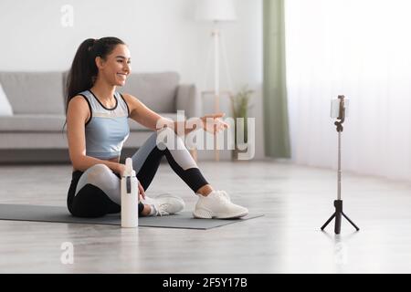 Jolie femme assise sur un tapis de yoga, ayant un appel vidéo Banque D'Images