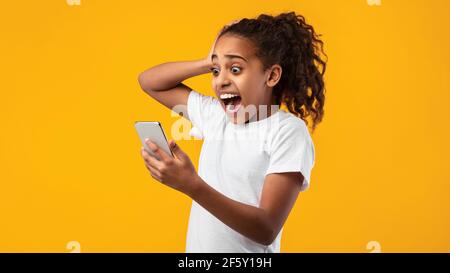 Une fille noire inquiète et effrayée regardant le téléphone voyant de mauvaises nouvelles Banque D'Images