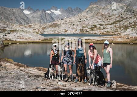 Des amies souriantes avec des chiens debout à Titcomb Basin on jour ensoleillé Banque D'Images