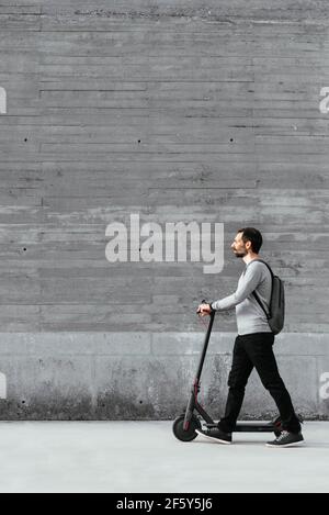 Homme marchant près d'un scooter électrique devant le mur gris Banque D'Images