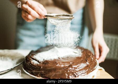 Anonyme femme versant du sucre en poudre sur le gâteau au chocolat Banque D'Images