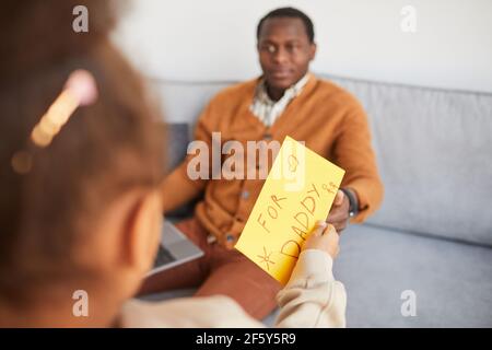 Gros plan d'une fille afro-américaine méconnue qui donne un cadeau surprise à papa le jour des Pères, espace copie Banque D'Images