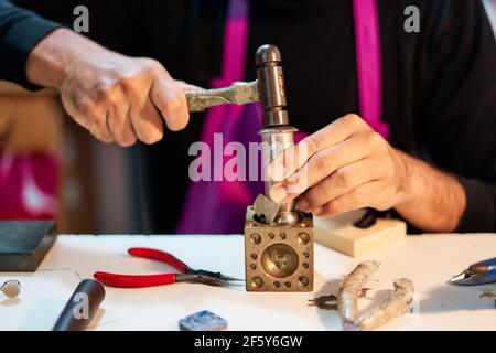 Gros plan artisan bijoutier frapper une plaque métallique avec le marteau sur la table de travail Banque D'Images