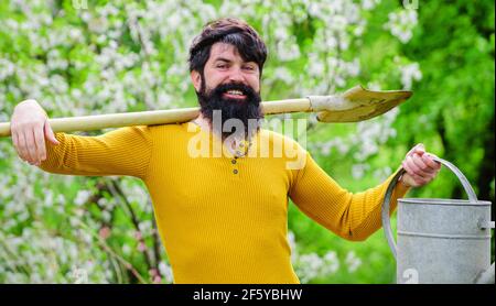 Heure de printemps. Jardinier souriant avec arrosoir et bêche. Arrosage. Travail dans le jardin. Banque D'Images