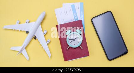 Miniature d'un avion, billets d'avion avec passeport et une montre sur fond jaune. Concept de temps pour le voyage Banque D'Images