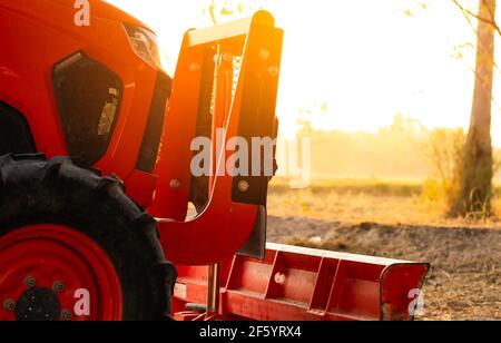 Tracteur orange stationné à la ferme de riz en été le matin avec la lumière du soleil. Machines agricoles dans l'agriculture agricole. Concept d'agriculture intelligente. Véhicule dans la ferme Banque D'Images