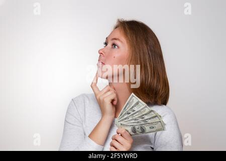 Finance et banque. Une jeune blonde tient une wad de dollars dans ses mains et regarde soigneusement loin. Vue de profil. Copier l'espace. Banque D'Images