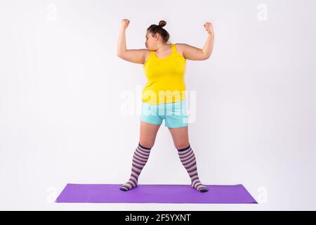 Fitness à domicile, entraînement en ligne avec un ordinateur portable couleur gris ultime. Embonpoint, plump femme regardant tutoriel vidéo faire stretching exerciseon tapis de fitness Banque D'Images