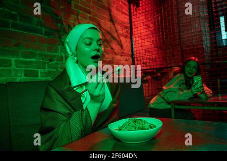 Belle fille avec une boucle d'oreille de perle prenant le déjeuner dans un café moderne, restaurant à la lumière du néon Banque D'Images