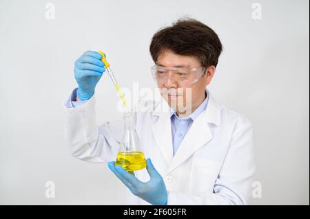 Portrait d'un scientifique asiatique de milieu d'année portant une blouse de laboratoire blanche et des gants et tenant un conteneur expérimental dans la main. Banque D'Images