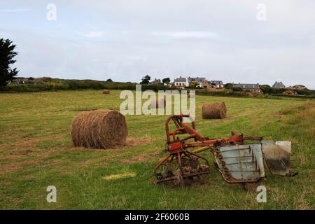 Un champ sur la partie nord de l'Île-de-Bréhat, Côtes d'Armor, Bretagne, France : machines agricoles abandonnées et balles de paille Banque D'Images