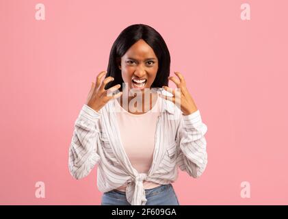 Une femme noire en colère criait à haute voix, fatiguée de ses problèmes, exprimant des émotions négatives sur fond rose studio Banque D'Images