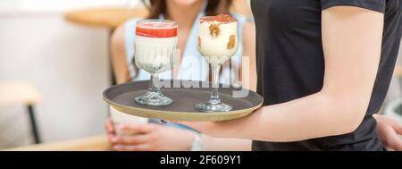 Une jeune serveuse portant un plateau avec deux desserts différents dans un café à deux verres Banque D'Images