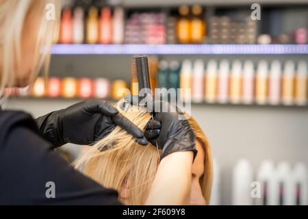 Coiffeur peignant les cheveux féminins du client avant de teindre les cheveux dans un salon de coiffure Banque D'Images