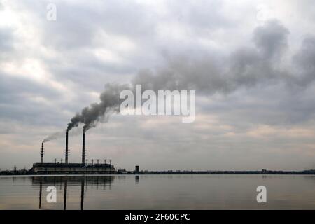 Centrale à charbon haute tuyauterie avec fumée noire se déplaçant vers le haut atmosphère polluante avec des réflexions de lui dans l'eau du lac. Banque D'Images