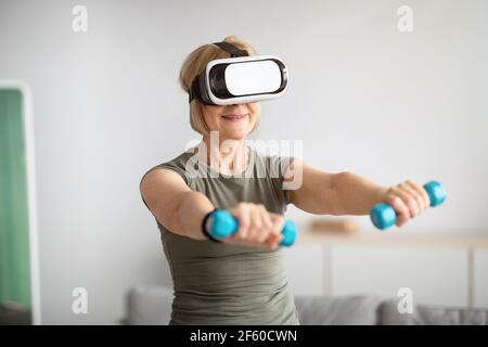 Concept d'entraînement virtuel. Posez la femme senior dans des lunettes VR en faisant des exercices avec des haltères à la maison Banque D'Images