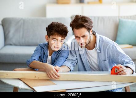 Père concentré et fils mesurant la planche de bois avec du ruban adhésif, homme enseignant garçon faisant des travaux ménagers Banque D'Images