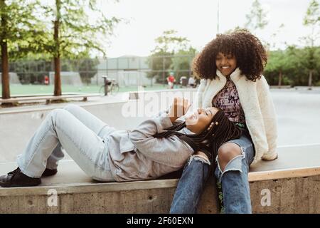 Une adolescente se repose la tête sur les genoux de ses amis pendant qu'elle est assise sur la retenue au parc de skateboard Banque D'Images