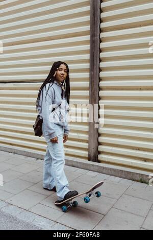 Adolescente avec planche à roulettes sur la piste de marche par un mur métallique Banque D'Images