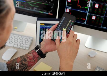 Image rapprochée d'un commerçant vérifiant les données du marché boursier via une application sur smartphone, achetant et vendant des actions Banque D'Images