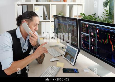 Trader professionnel vérifiant les données du marché boursier sur des écrans sur ordinateur et table numérique et passer un appel téléphonique Banque D'Images