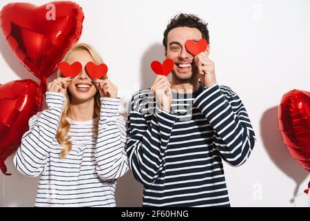 Joyeux jeune couple attrayant célébrant la Saint-Valentin avec cœur rouge bulles formées isolées sur fond blanc Banque D'Images