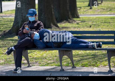 Un couple sur un banc de parc dans Flushing prés Corona Park. Il dort sur ses genoux et elle lit depuis son téléphone portable. Banque D'Images