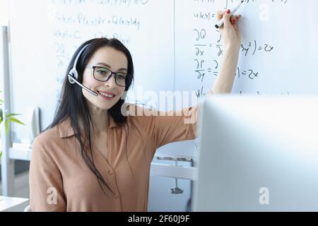 Femme dans un casque assis devant un ordinateur portable et montrant informations sur le tableau blanc Banque D'Images