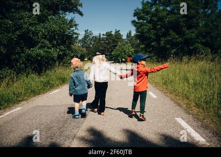 Vue arrière de la sœur avec les frères marchant sur la route pendant jour ensoleillé Banque D'Images