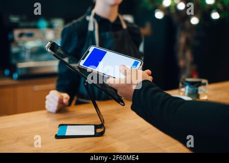 Main courte d'un client masculin effectuant un paiement sans contact via SMART téléphone à la cafétéria Banque D'Images