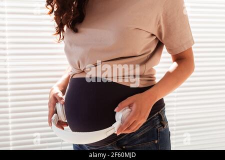 Les mains de la jeune femme enceinte mettent des écouteurs avec de la musique classique sur son ventre. Concept de développement intra-utérin intellectuel de l'enfant Banque D'Images