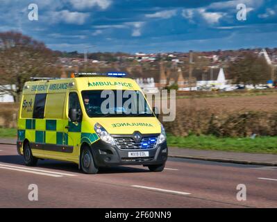 Une ambulance NHS voyageant à grande vitesse sur une route dans une zone semi-urbaine de l'Angleterre, au Royaume-Uni. Pris lors d'une journée ensoleillée et lumineuse avec un ciel bleu au printemps. Banque D'Images