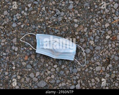 Un masque chirurgical bleu utilisé pour la protection EPI COVID-19, jeté comme litière sur une chaussée / un trottoir dans une zone urbaine Banque D'Images